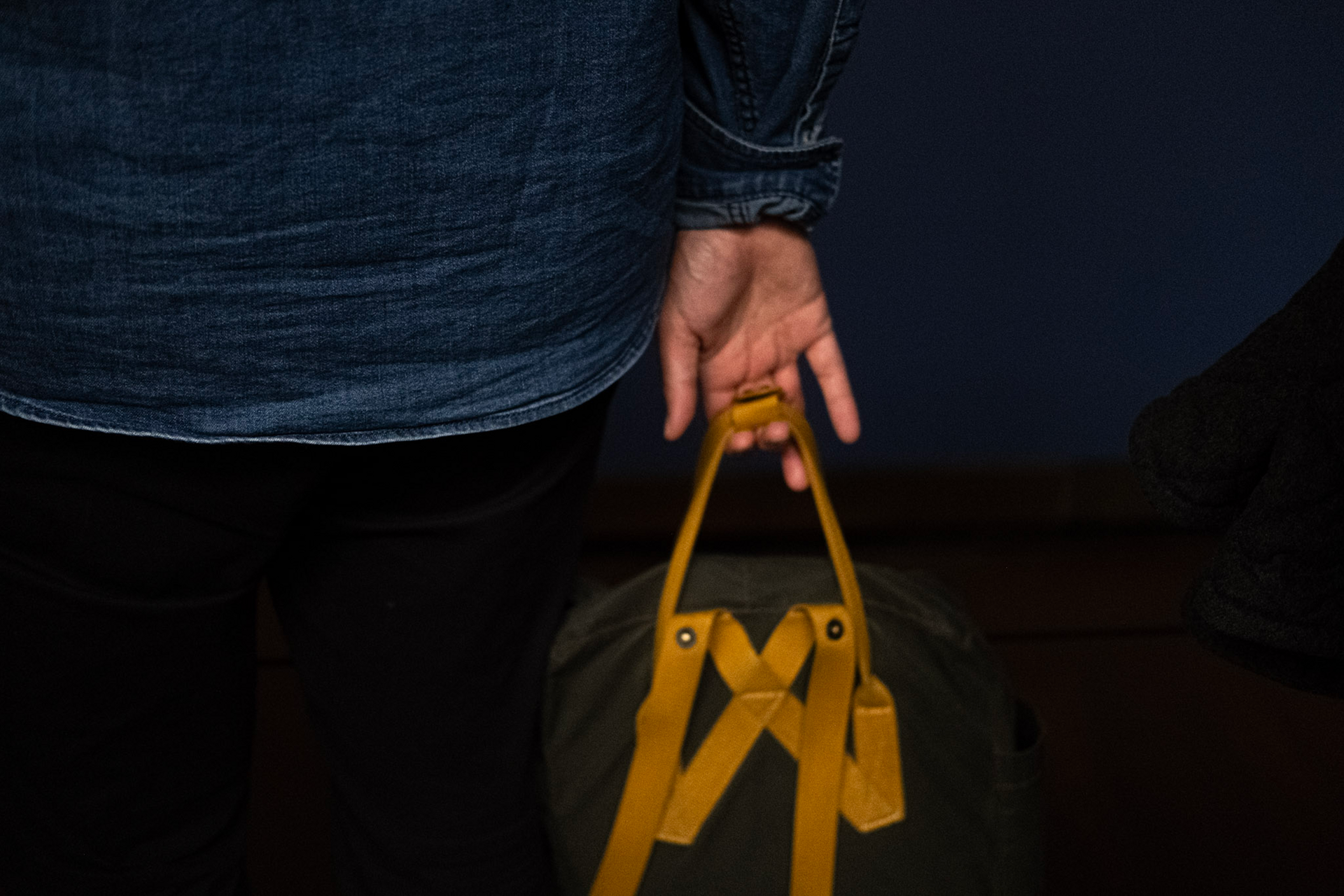 A hand carrying a canvas bag by its yellow straps, seen from behind